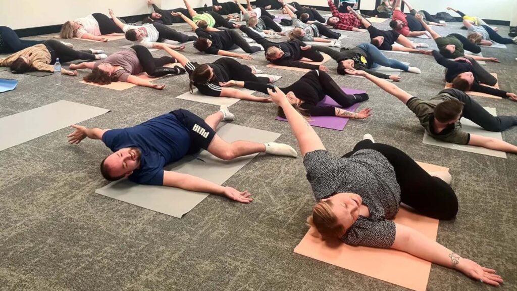 Large room with 20-30 people lying on their backs doing yoga