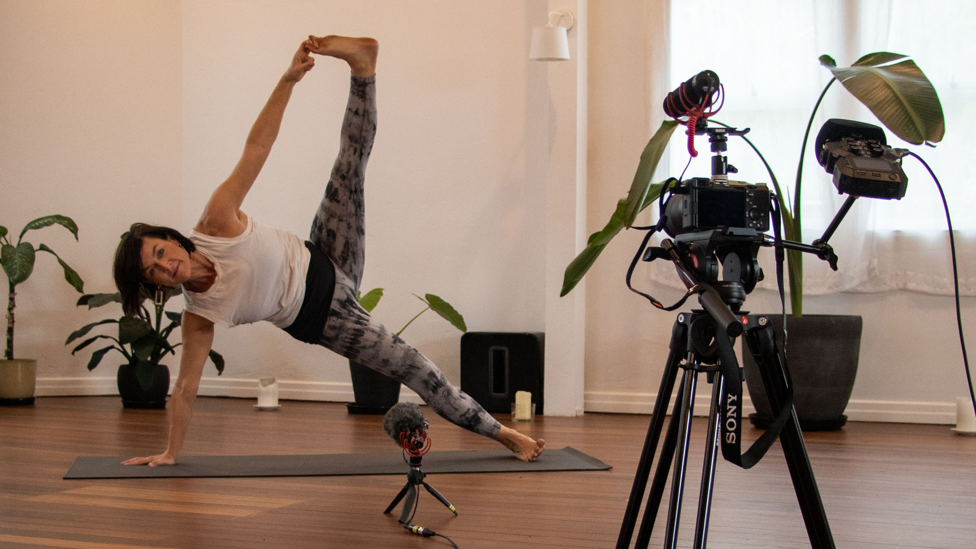 Debby Lewis demonstrating yoga pose in front of a camera and microphone in yoga studio