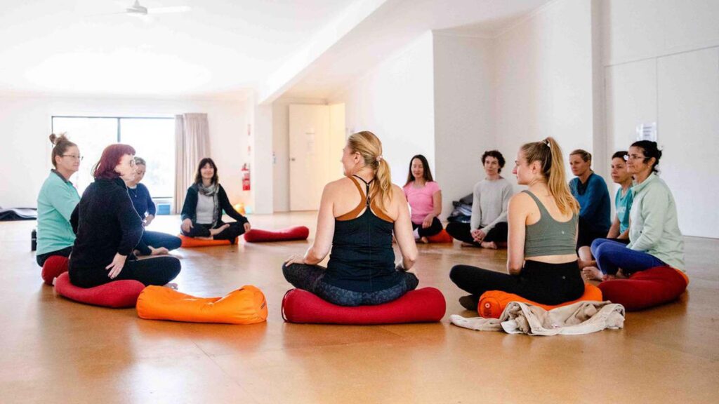 Circle of people in yoga class, sat on bolsters