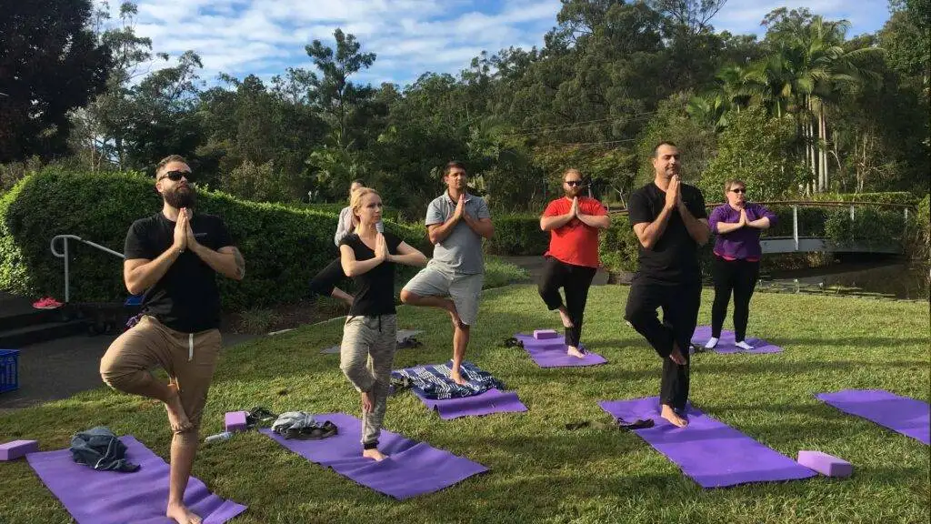Group of peope outside on grass doing yoga with a bridge in the background